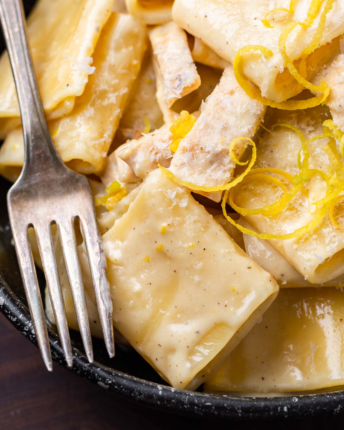 Creamy lemon chicken pasta in black bowl with lemon zest and cheese on top.