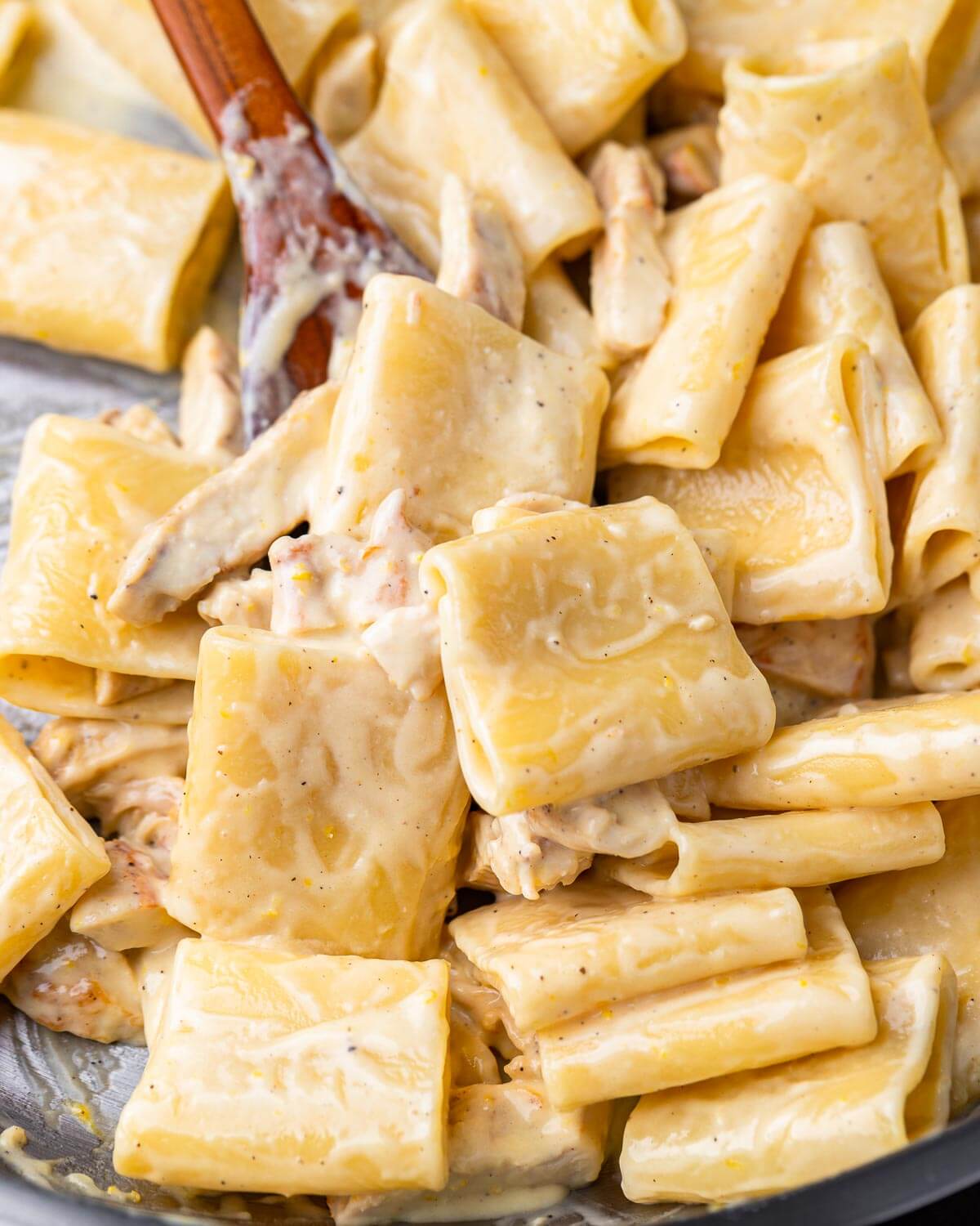 Creamy lemon chicken paccheri in pan with wooden spoon.