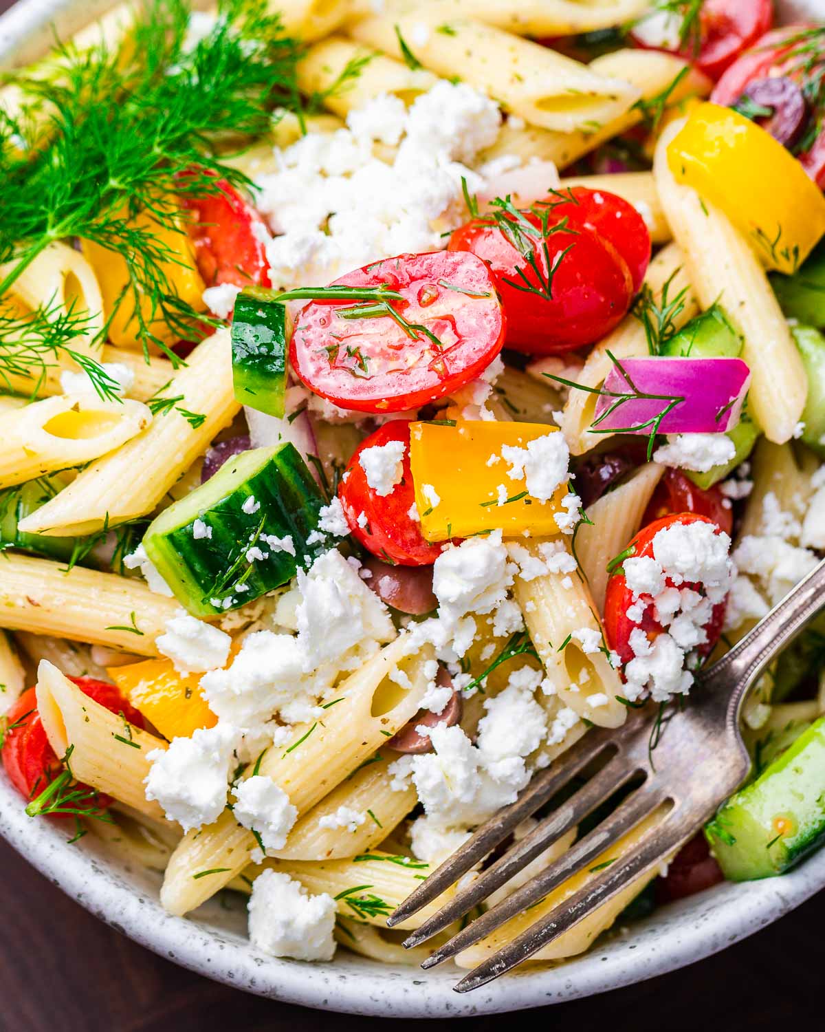 Closeup shot of Greek pasta salad in white bowl.