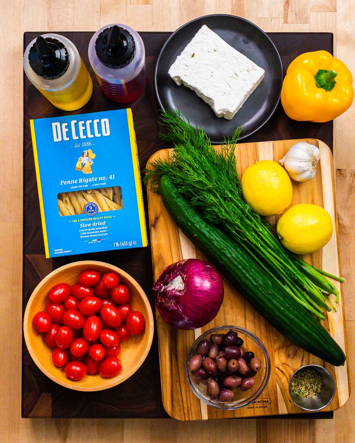Ingredients shown: oil, vinegar, feta, pepper, pasta, tomatoes, onion, olives, cucumber, dill, lemons, garlic, and oregano.