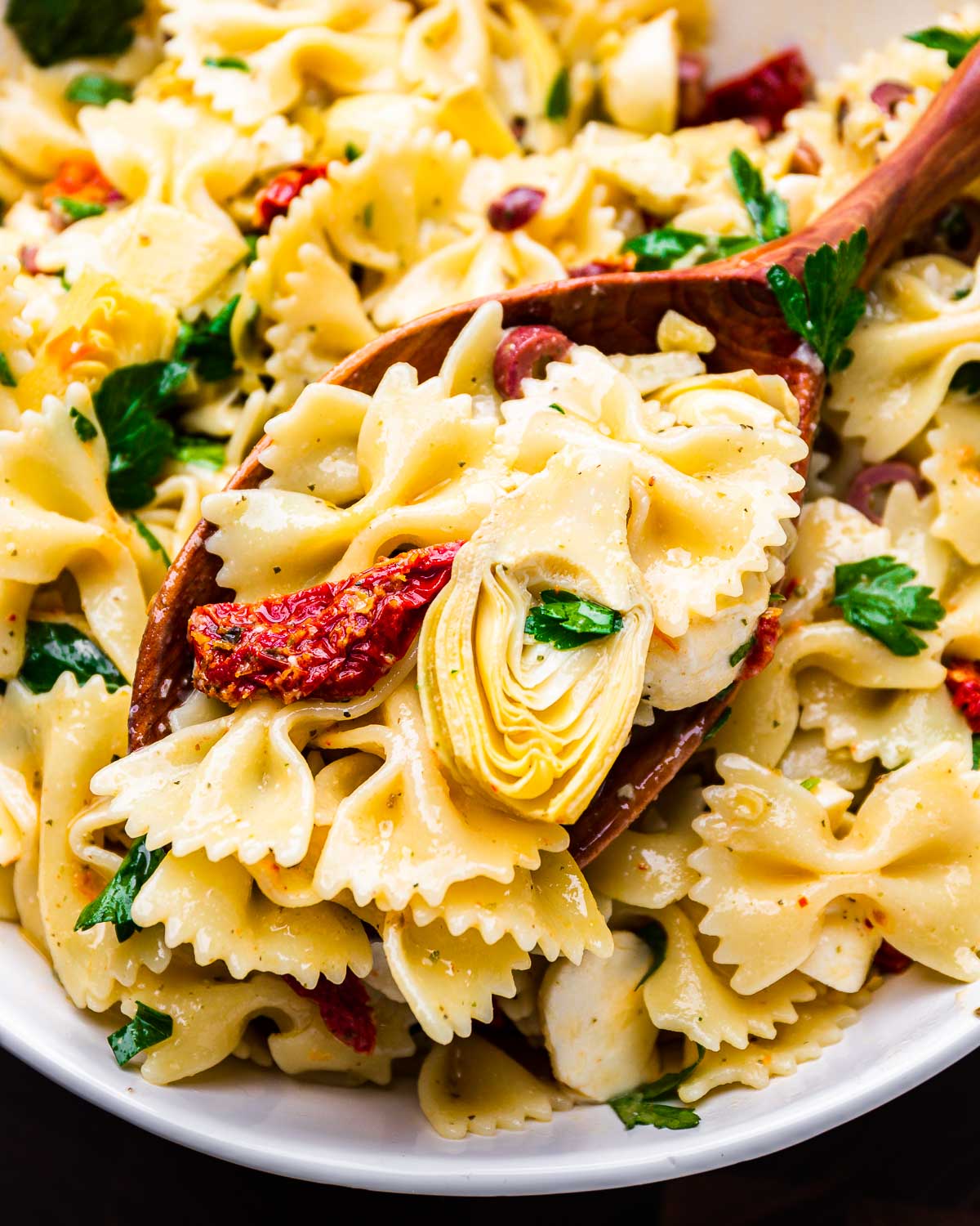 Large spoon holding scoop of artichoke heart sun dried tomato pasta salad.