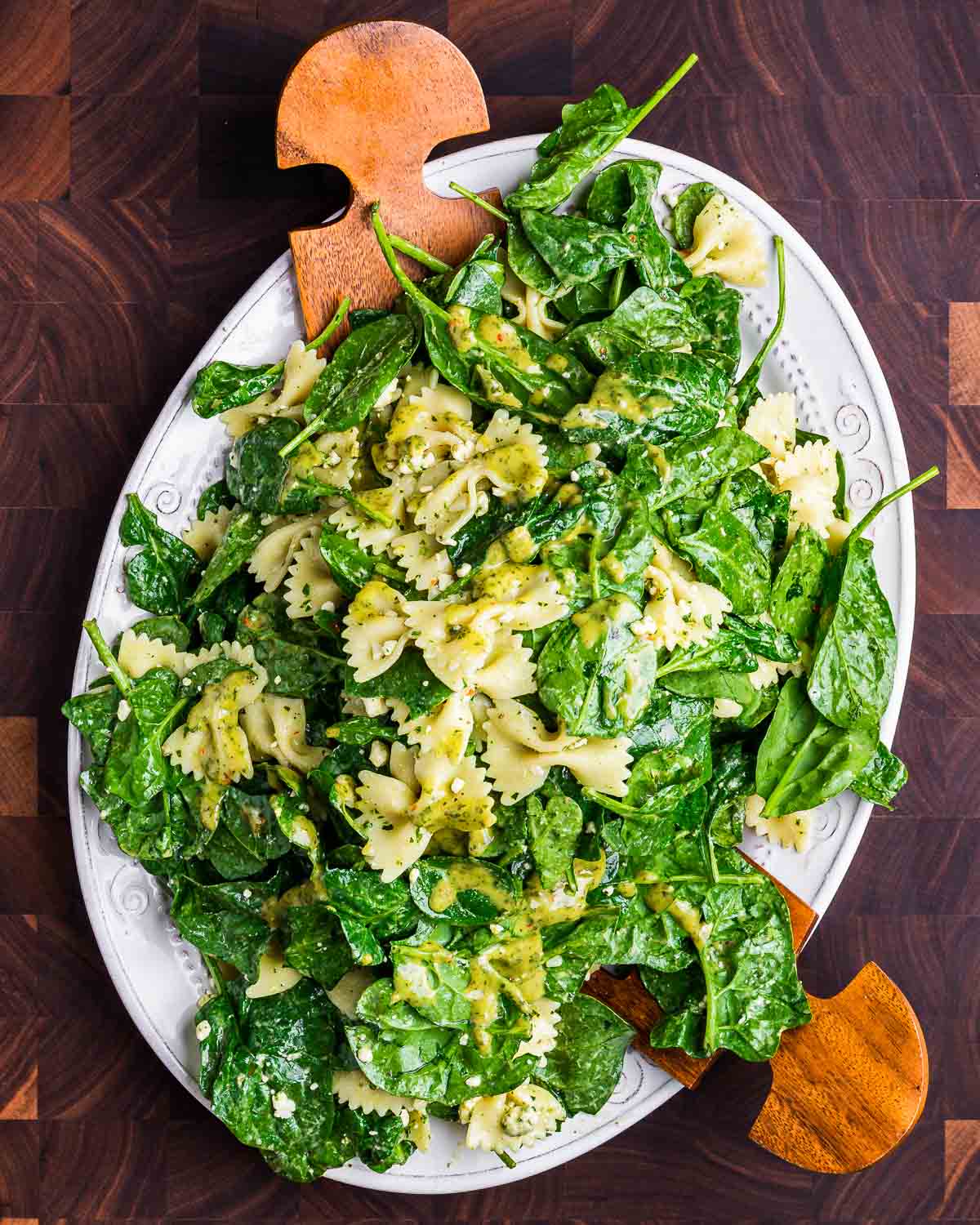 Spinach pasta salad in white platter on wood cutting board.