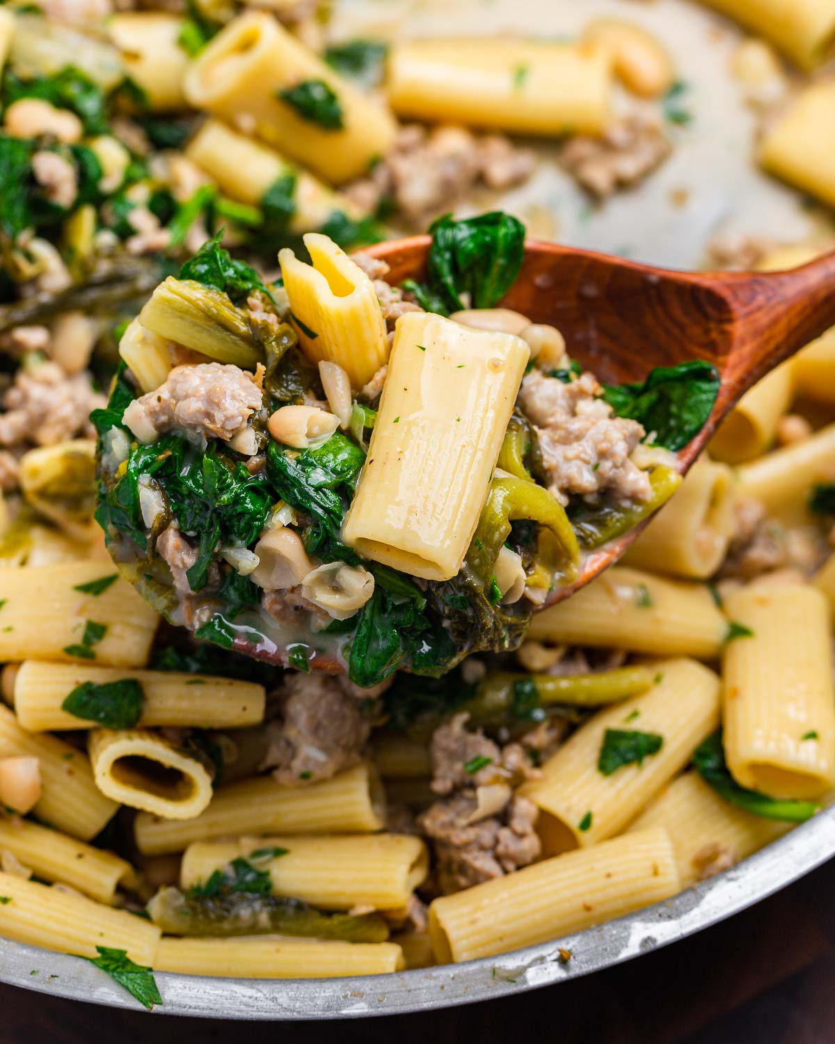 Large wooden ladle holding rigatoni with beans and greens.
