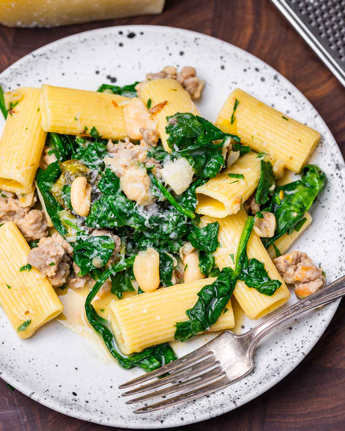 White plate with sausage beans and greens pasta.