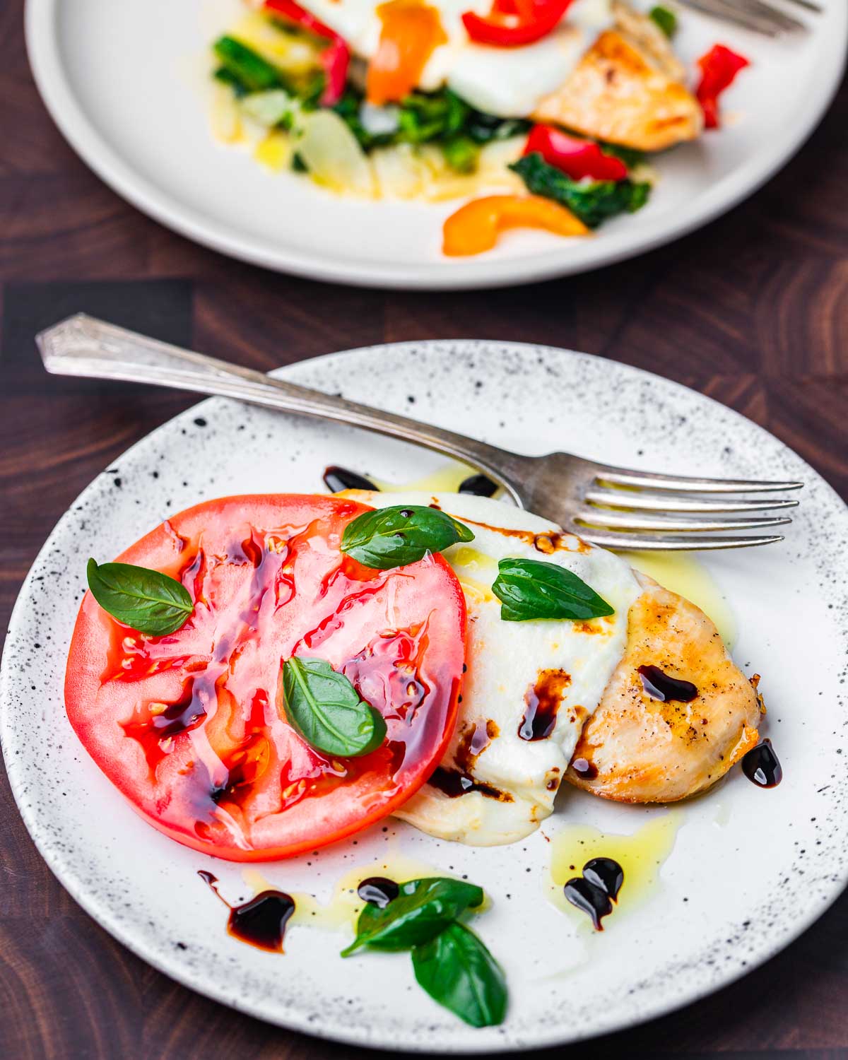 Chicken with mozzarella, tomato, basil, and balsamic glaze in white plate.