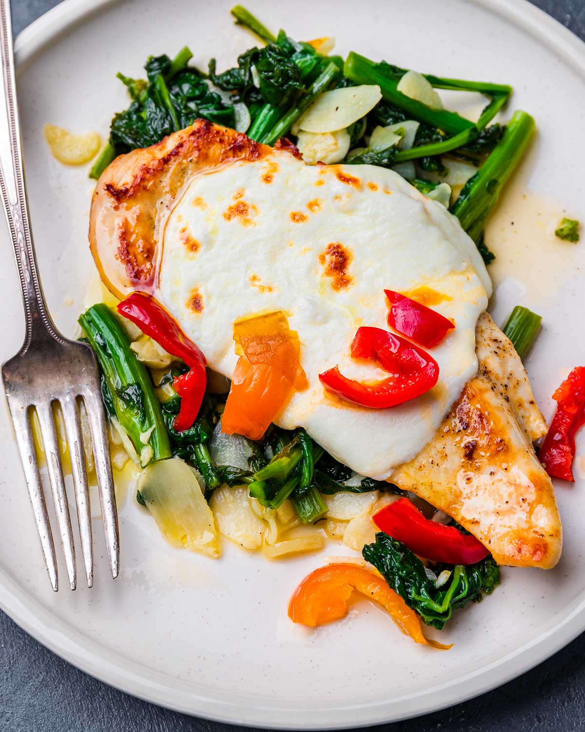 Chicken and broccoli rabe with cherry peppers in white plate.