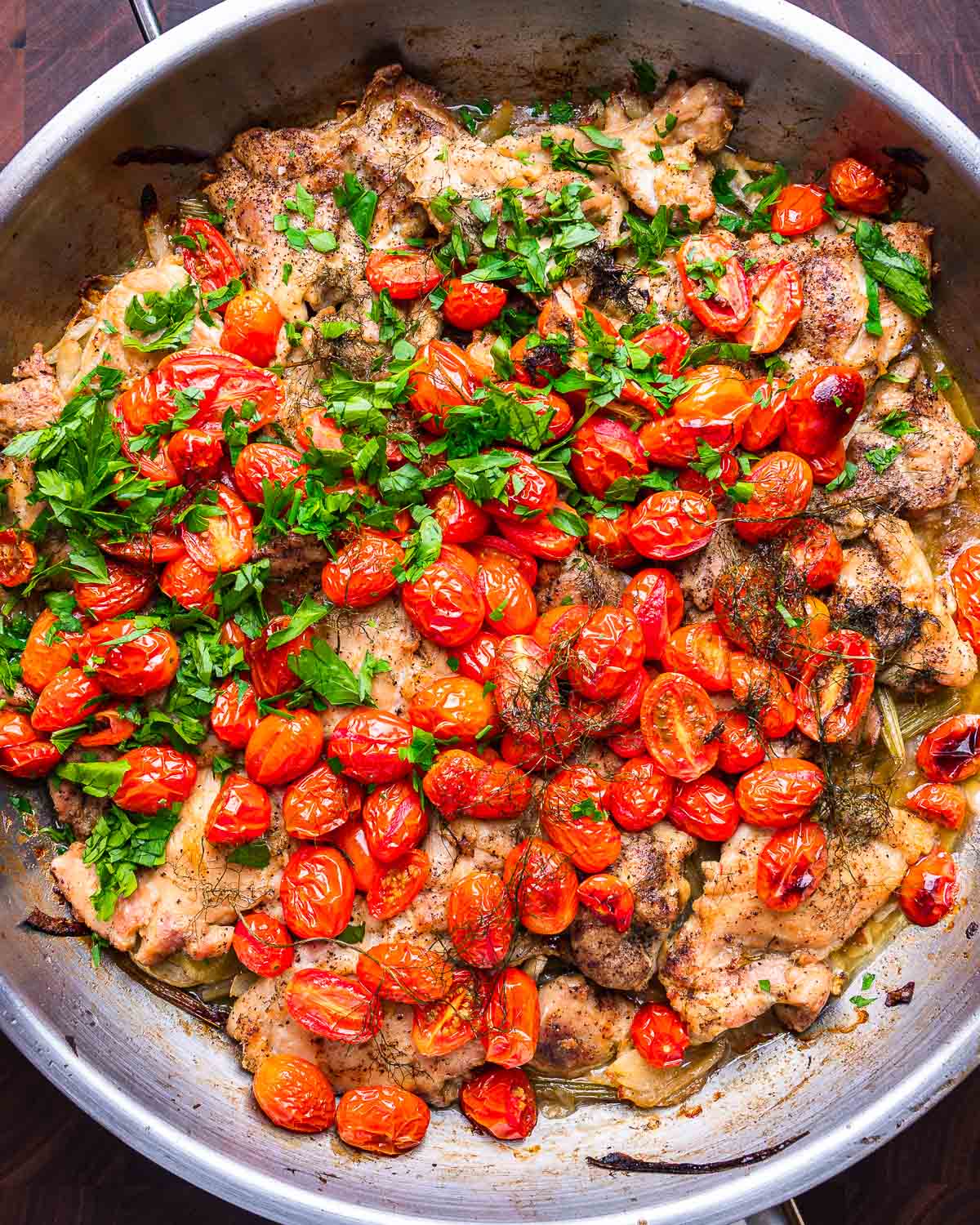 Overhead shot of chicken thighs with fennel and cherry tomatoes in large pan.