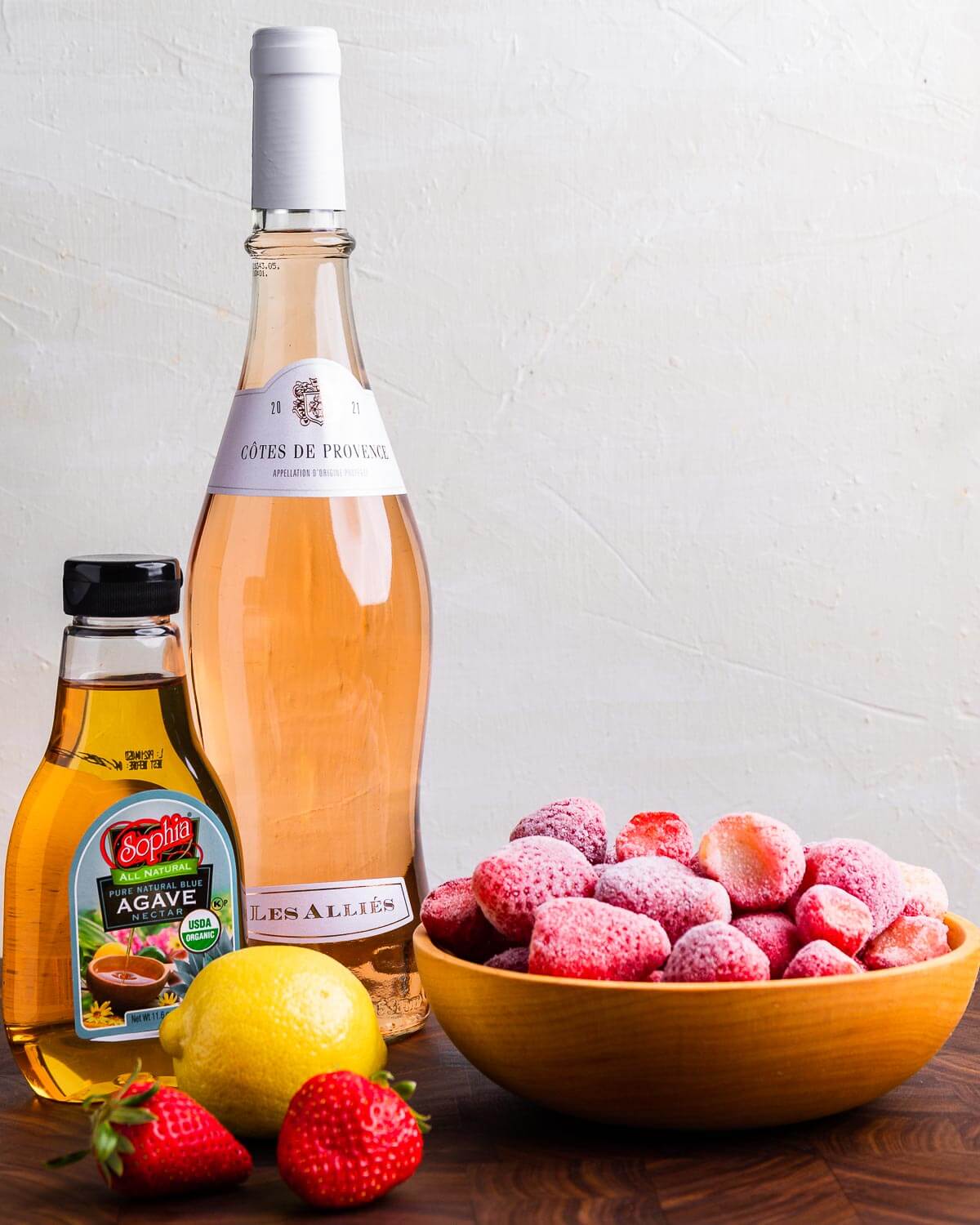 Ingredients shown: rosé wine, agave, frozen and fresh strawberries, and a lemon.