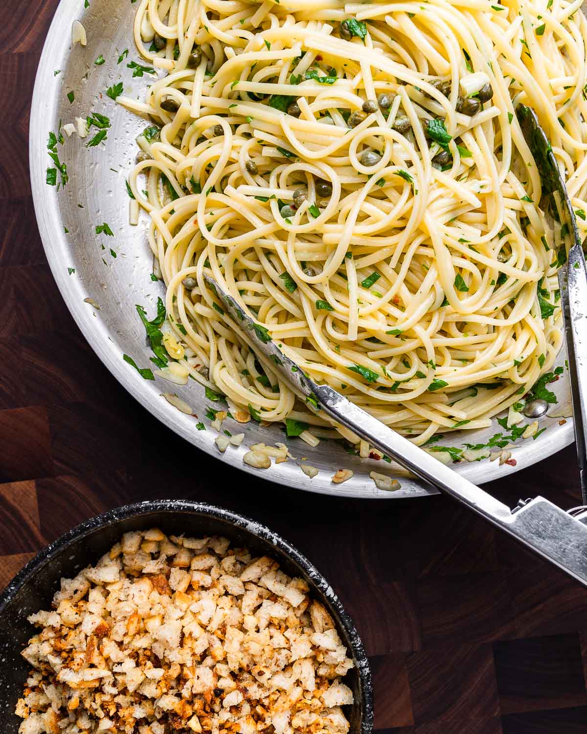 Overhead shot lemon caper linguine in pan and bowl of breadcrumbs.