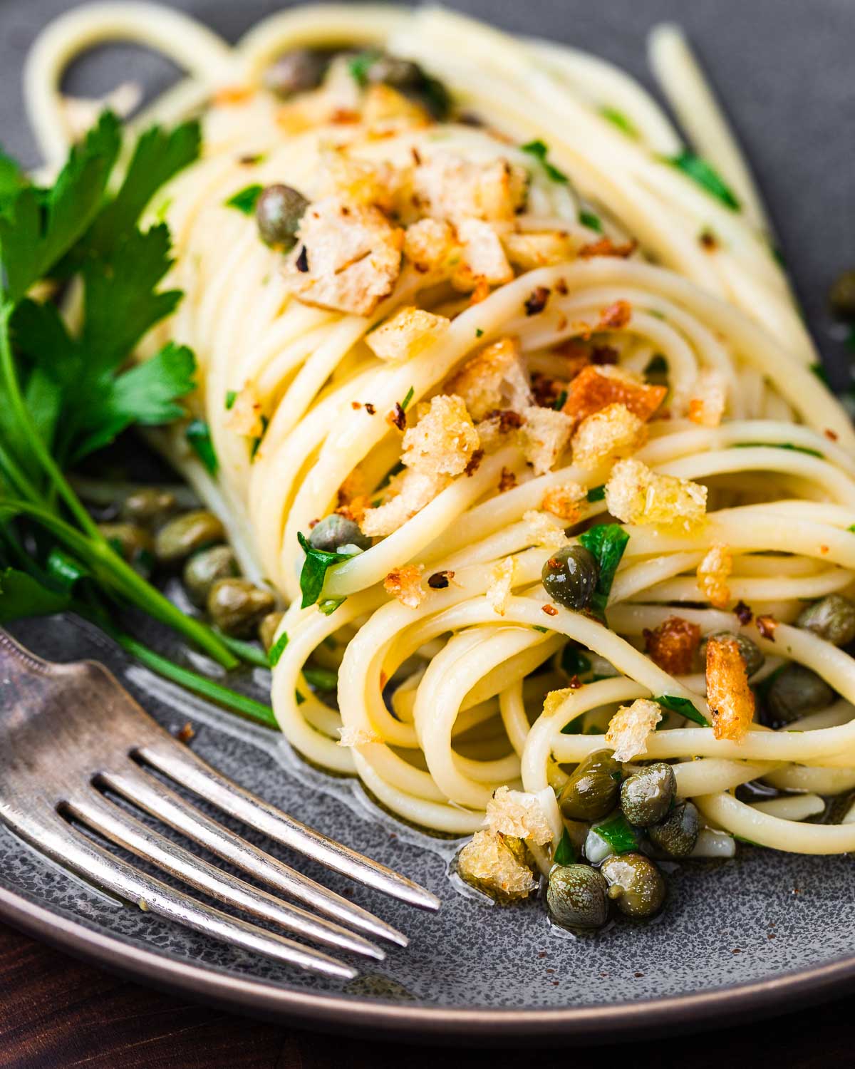 Lemon caper pasta in grey plate with fork.