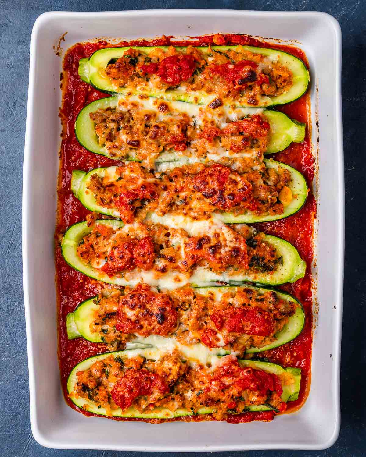 Overhead shot of sausage stuffed zucchini boats in white baking dish.