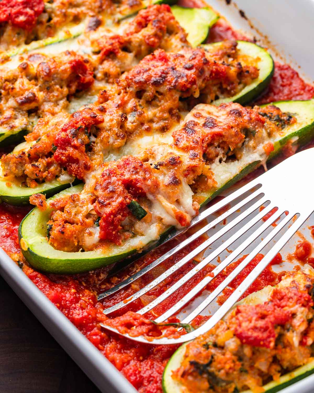 Sausage stuffed zucchini boats in white baking dish with spatula.