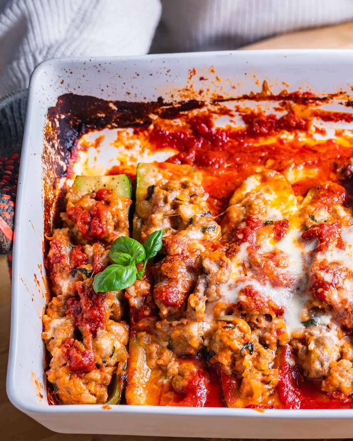 Person holding baking dish with sausage stuffed zucchini boats.