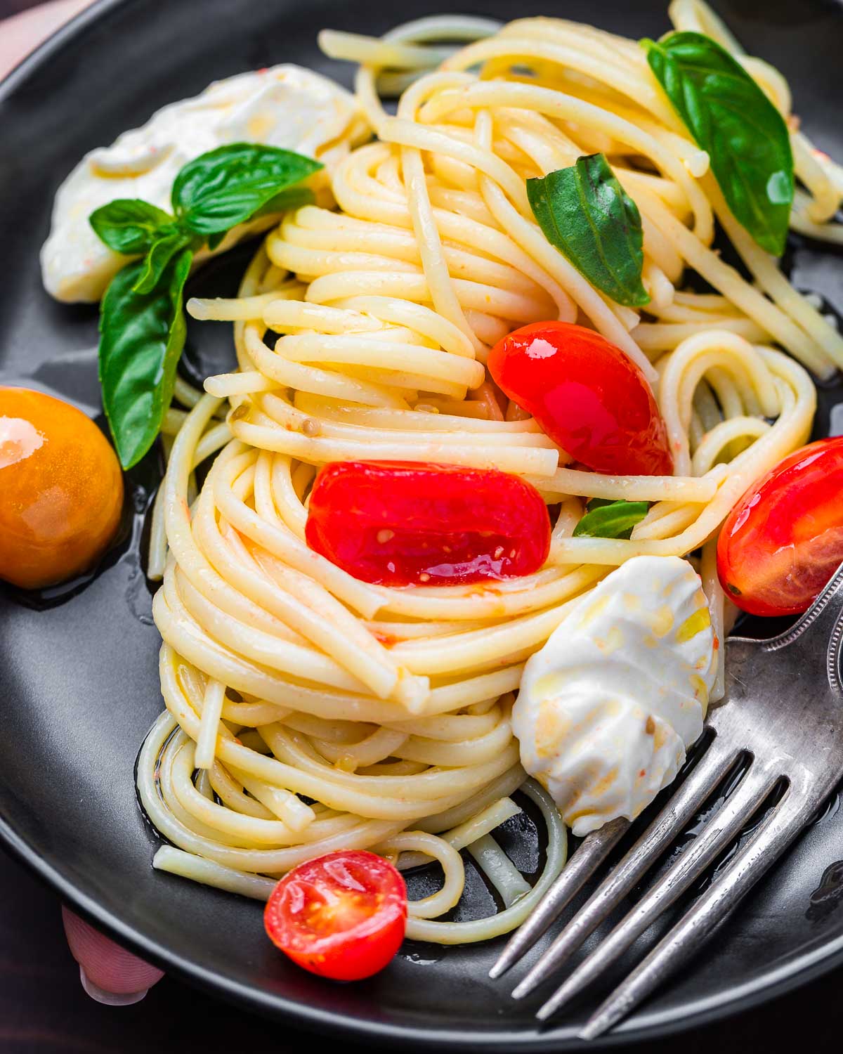 Hands holding caprese pasta in black plate.
