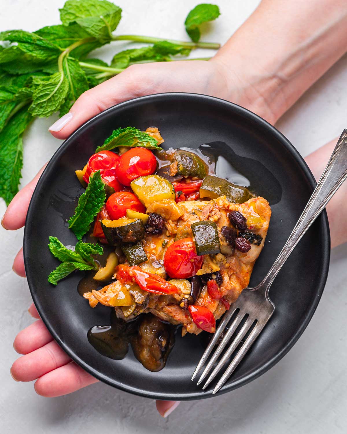 Hands holding chicken agrodolce in black plate.