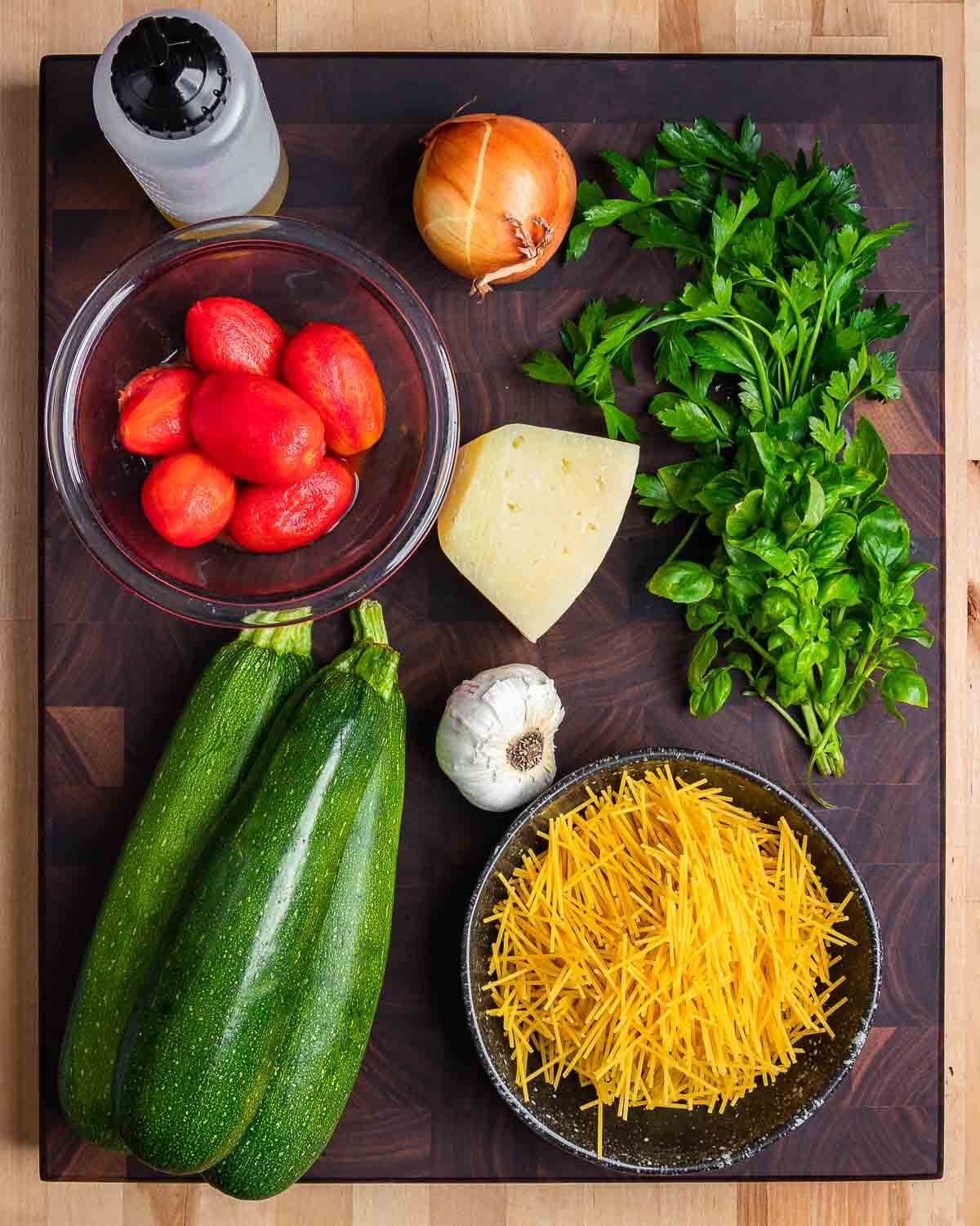 Ingredients shown: olive oil, plum tomatoes, onion, Pecorino, parsley, basil, garlic, zucchini, and broken spaghetti.