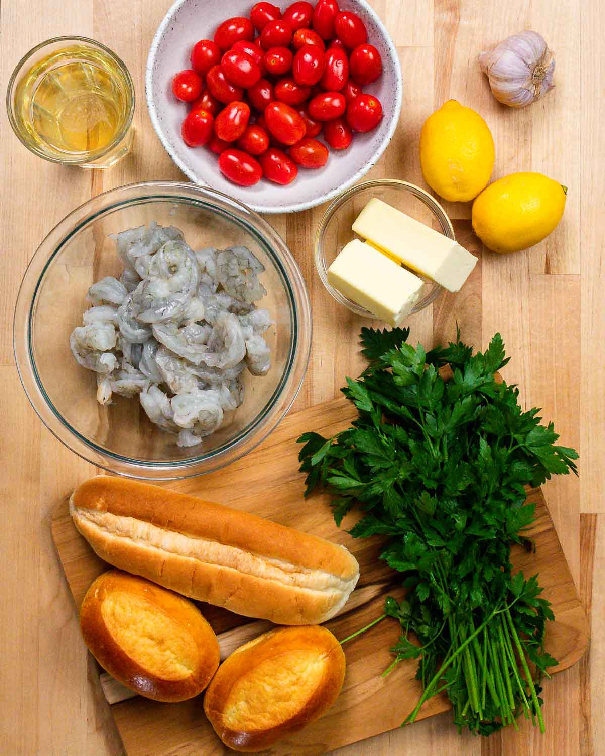 Ingredients shown: white wine, tomatoes, garlic, lemon, butter, shrimp, rolls, and parsley.