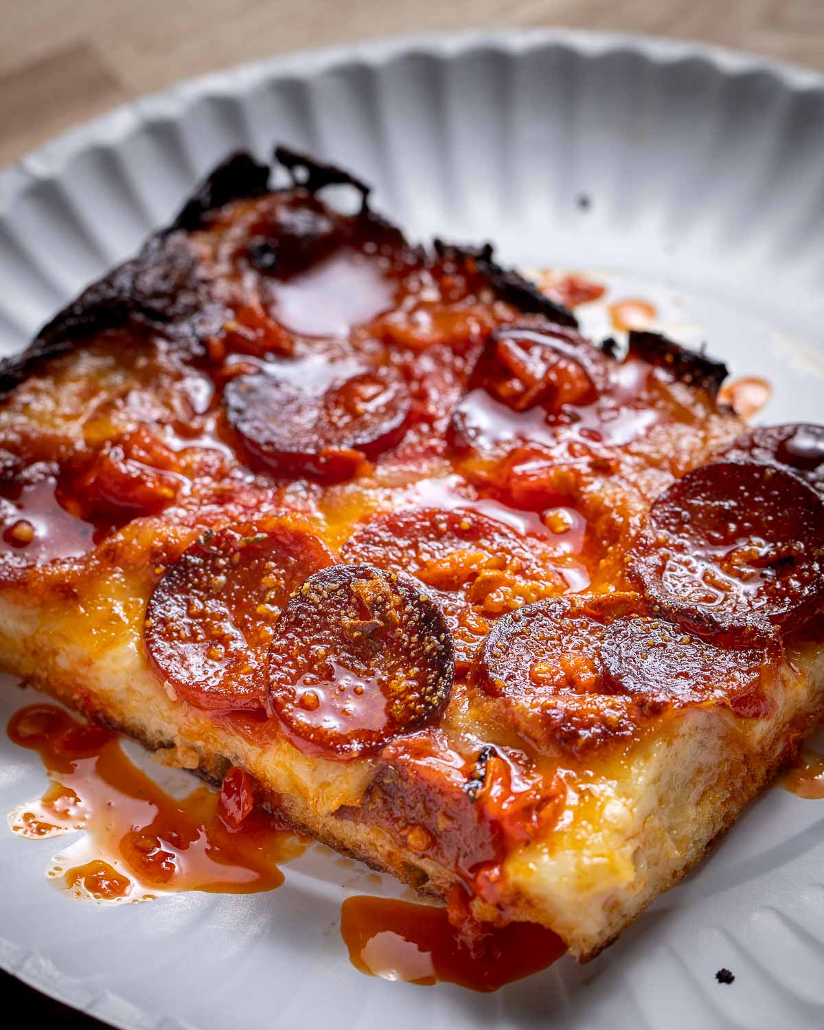 Slice of pepperoni pizza in white paper plate.