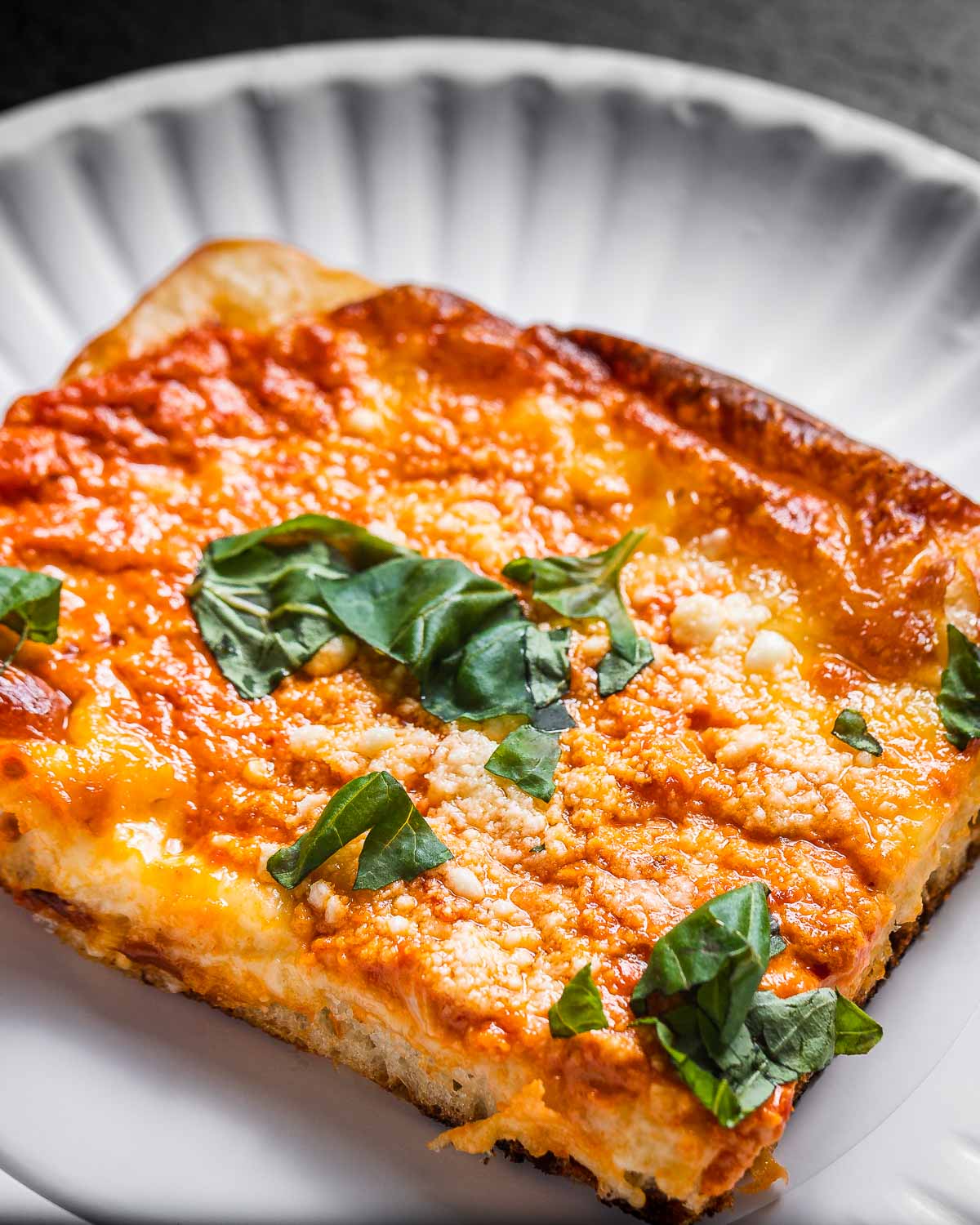 Slice of vodka sauce pizza in white paper plate.