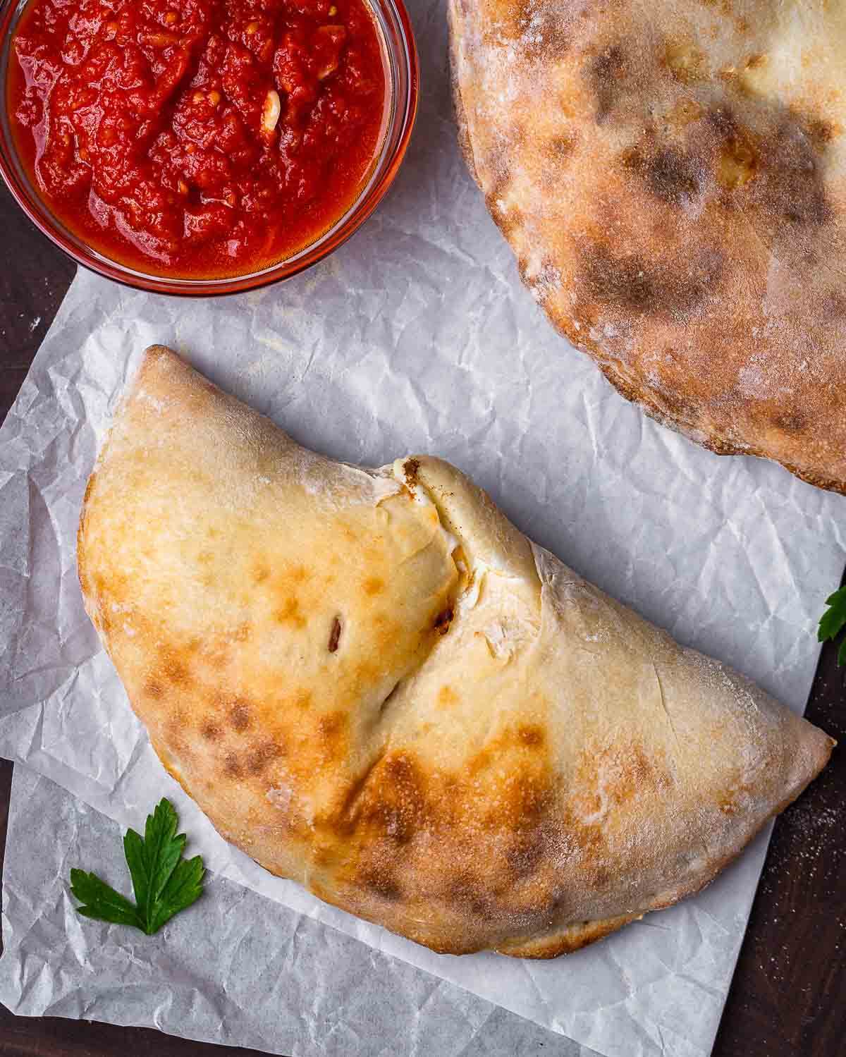 Overhead shot of 2 calzones and a small bowl of marinara sauce.