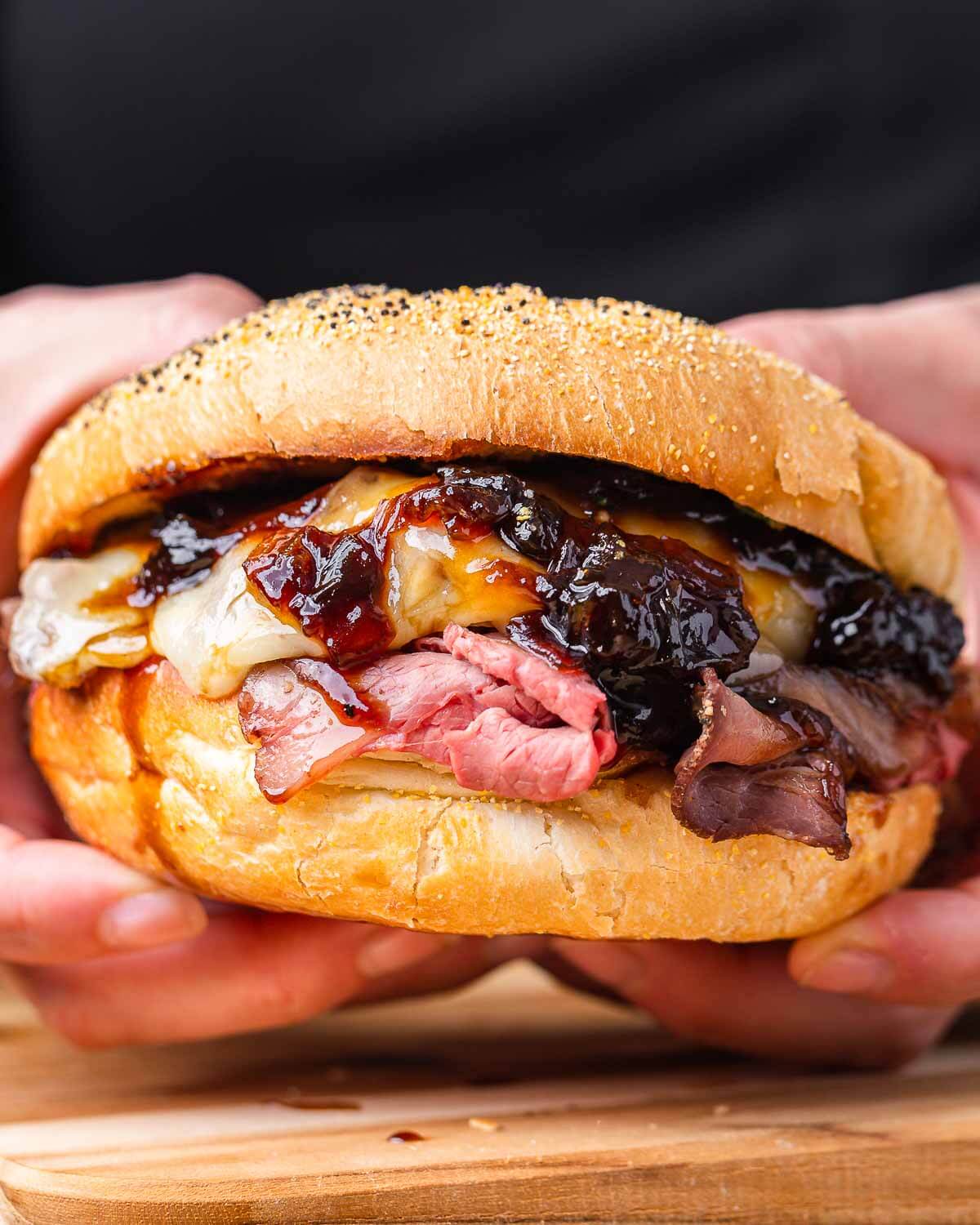 Hands holding roast beef sandwich with onion jam.