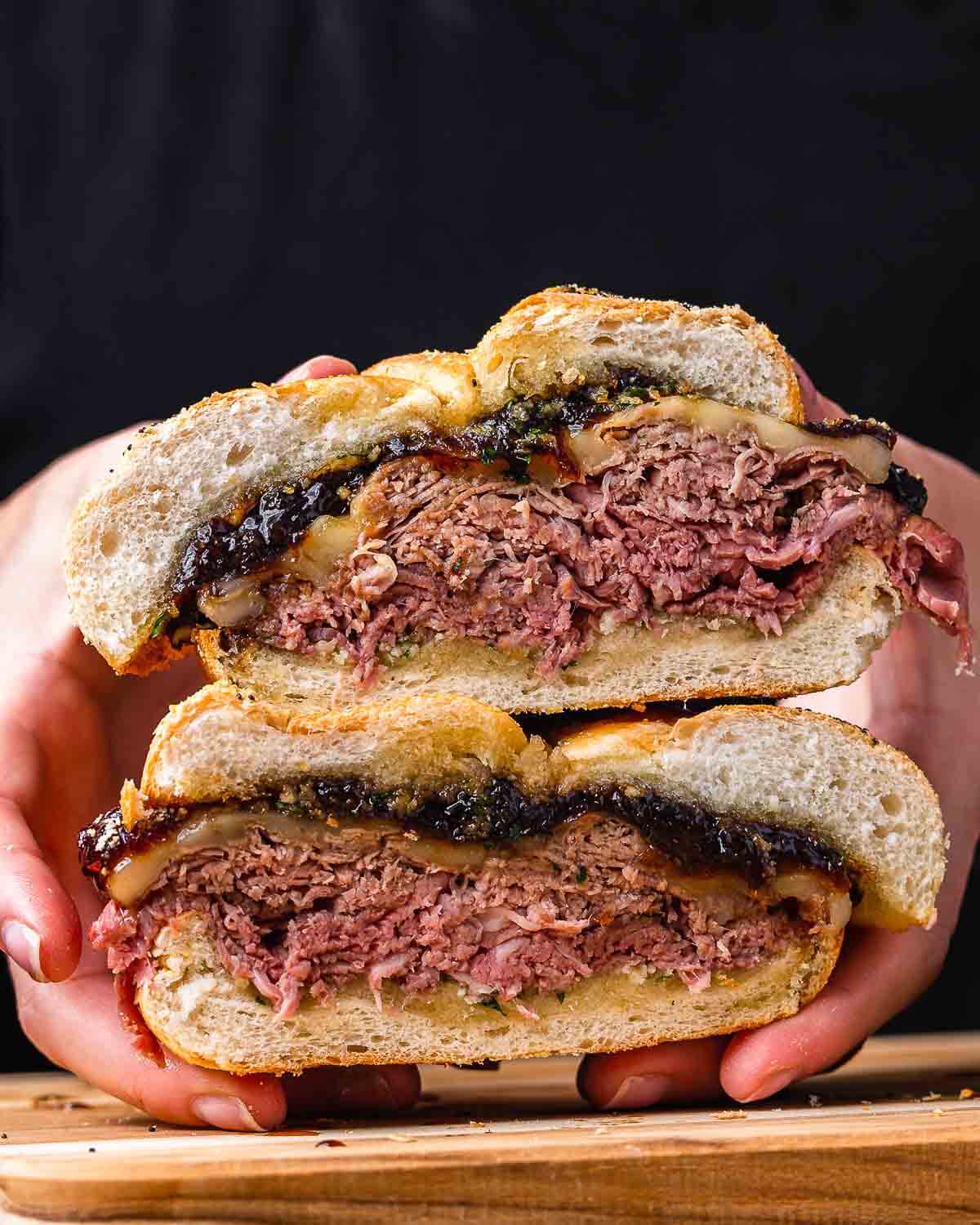 Hands holding cut in half roast beef sandwich.