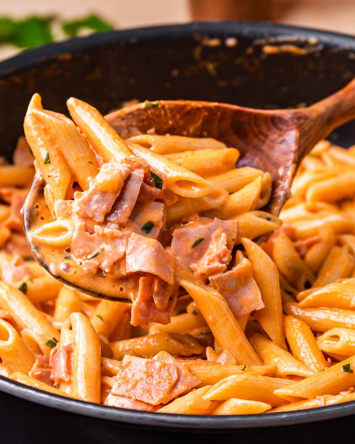 Wooden spoon holding penne with ham.