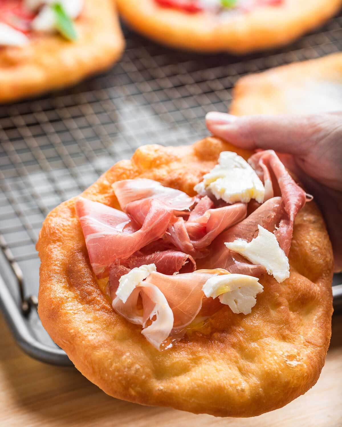 Hands holding pizza fritta with prosciutto and fresh mozzarella.