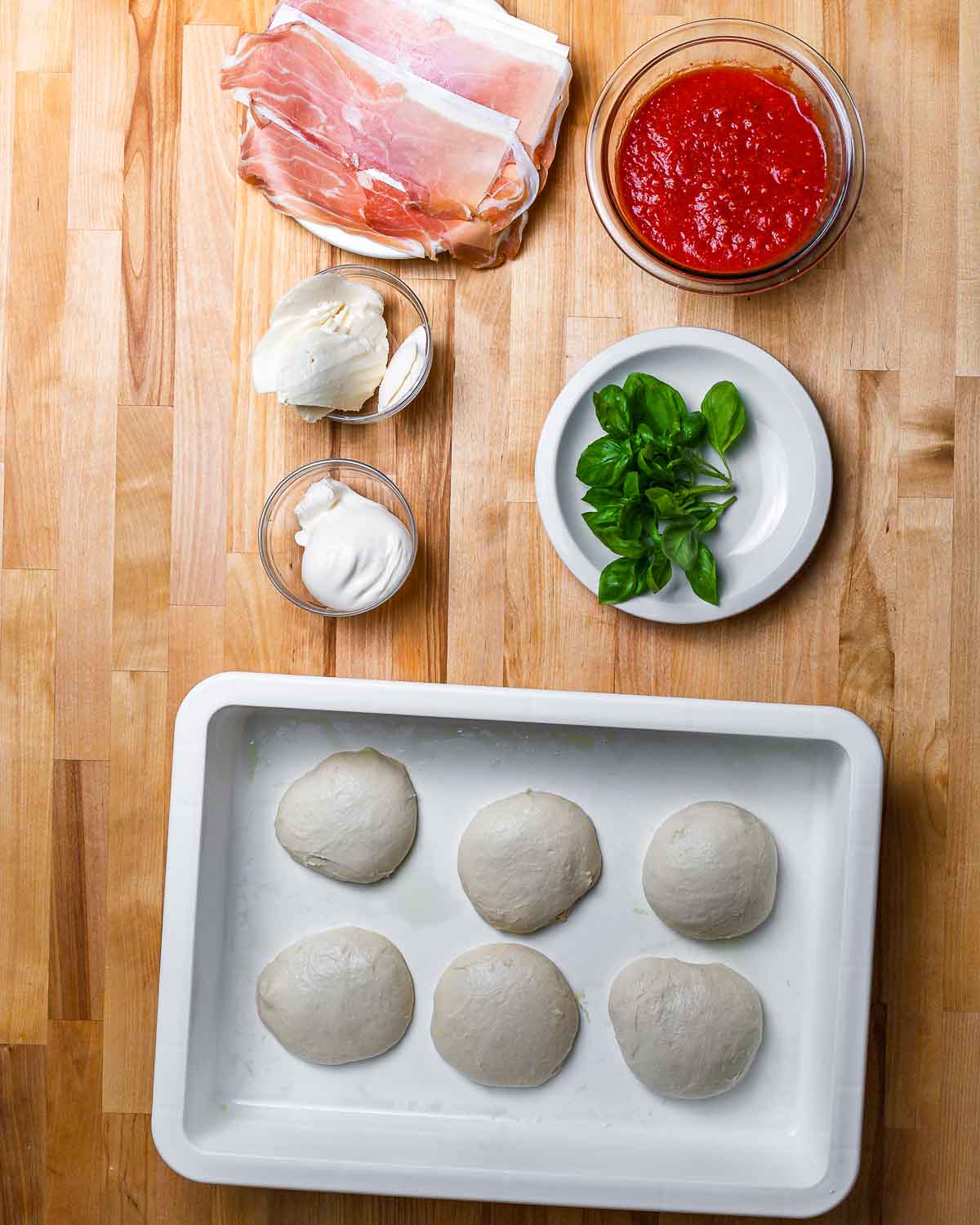 Ingredients shown: prosciutto, tomato sauce, mozzarella, burrata, basil, and 6 small dough balls.