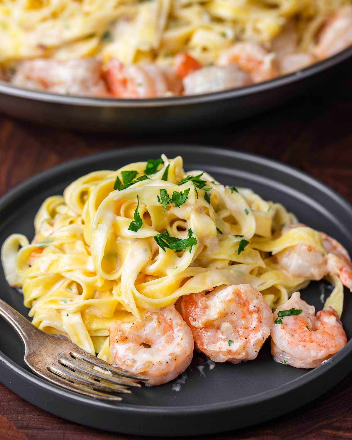 Shrimp alfredo in grey plate with large pan in background.