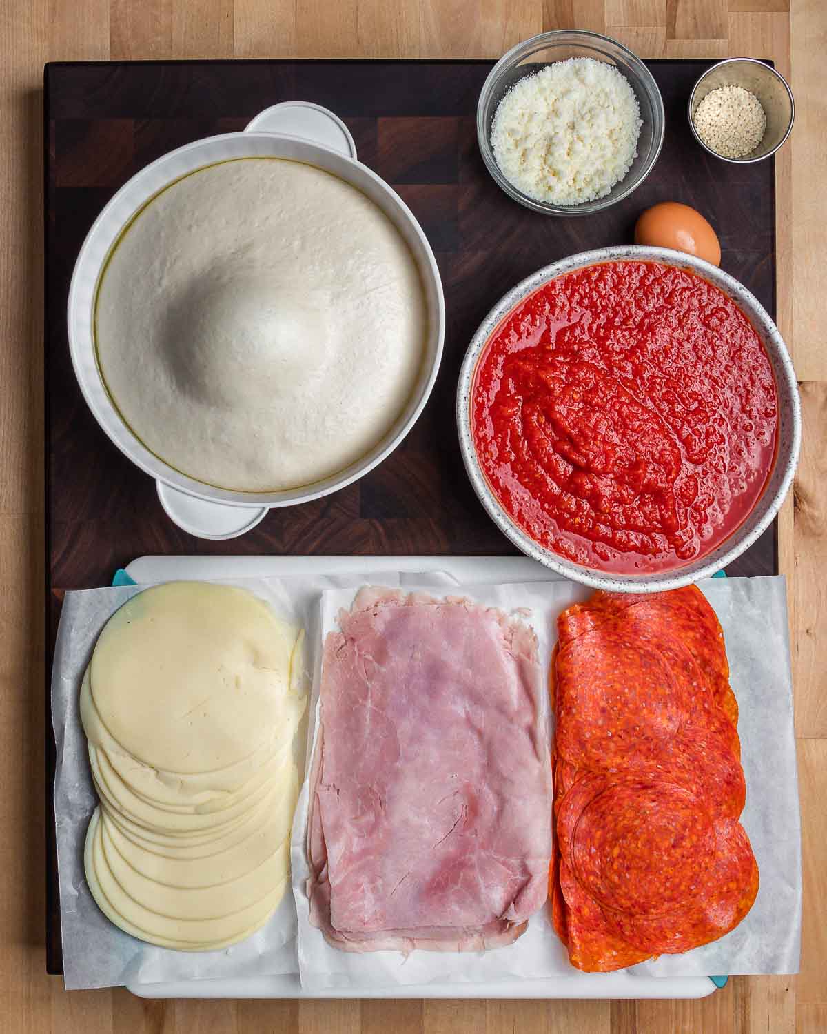 Ingredients shown: pizza dough, Pecorino, sesame seeds, 1 egg, marinara sauce, provolone, ham, and pepperoni.