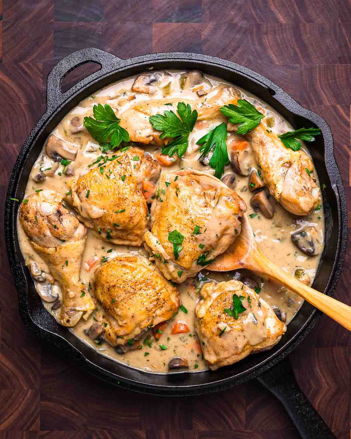 Overhead shot of chicken fricassee in cast iron pan with curved wooden spoon.