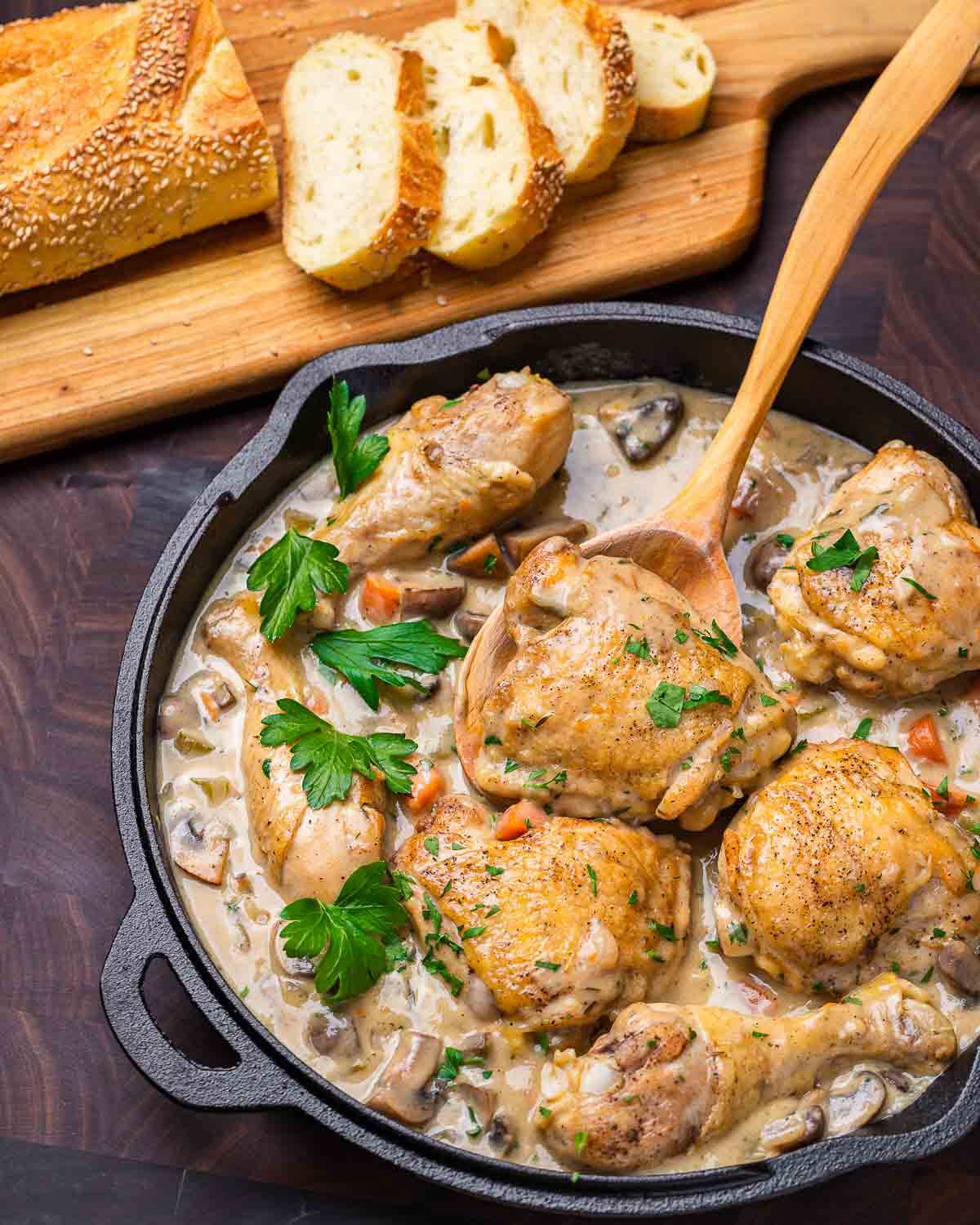 Chicken fricassee in cast iron pan and loaf of cut Italian bread.