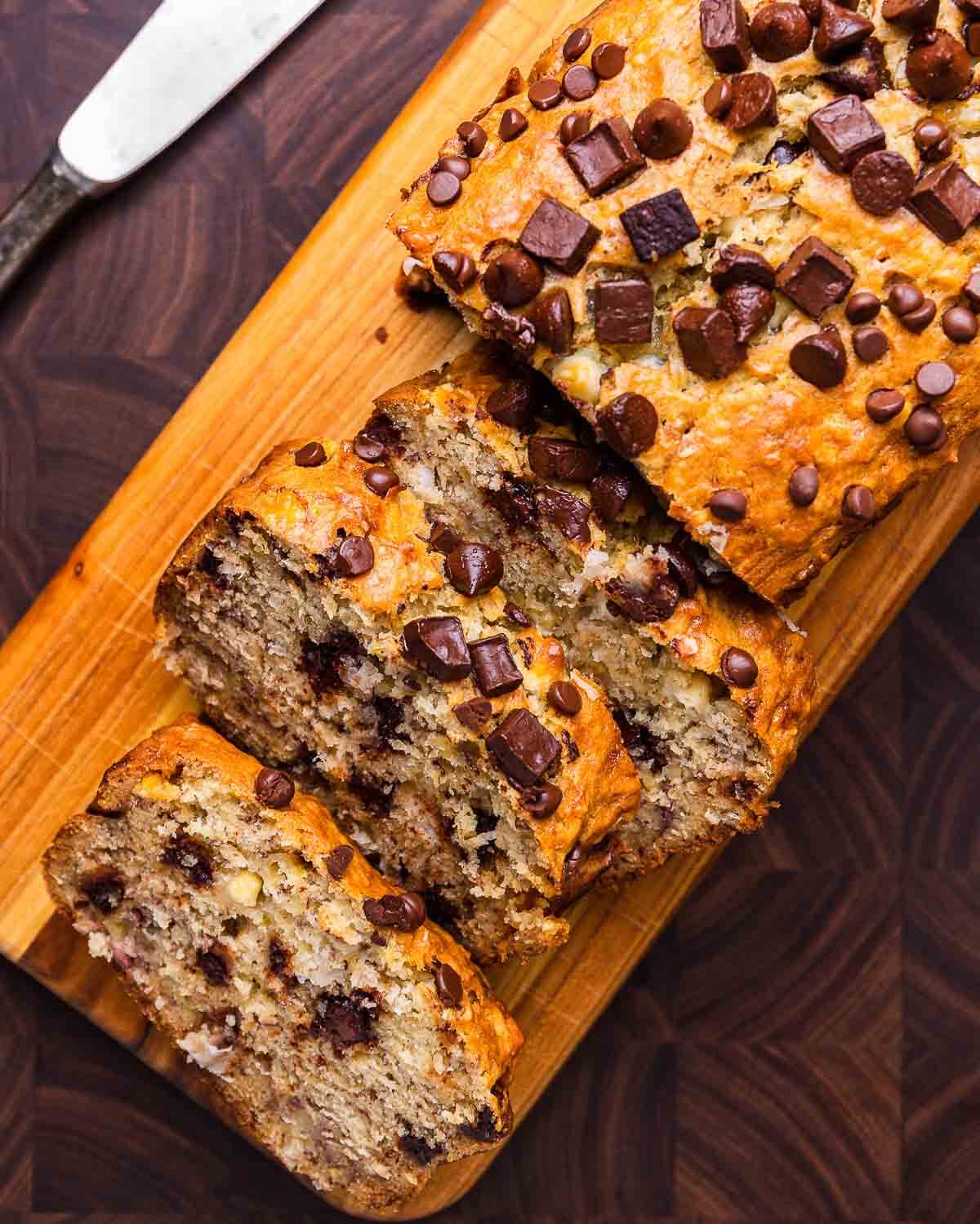Sliced chocolate chip banana bread on small wood serving board.