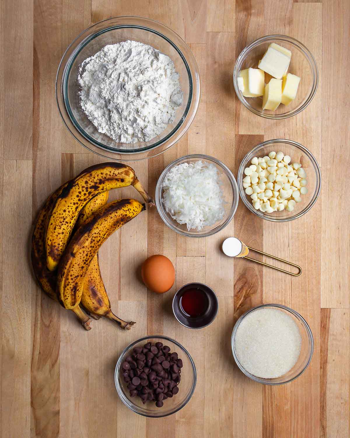 Ingredients shown: flour, butter, bananas, egg, coconut, white chocolate chips, sugar, vanilla, chocolate chops, and sugar.