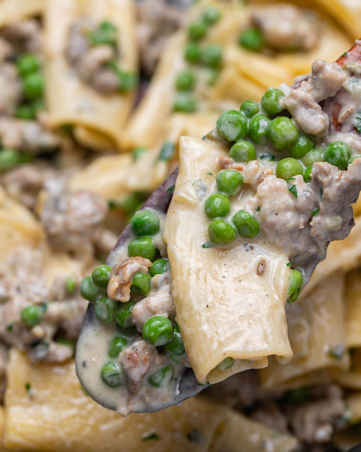 Wooden spoon holding one piece of rigatoni with peas and sausage.