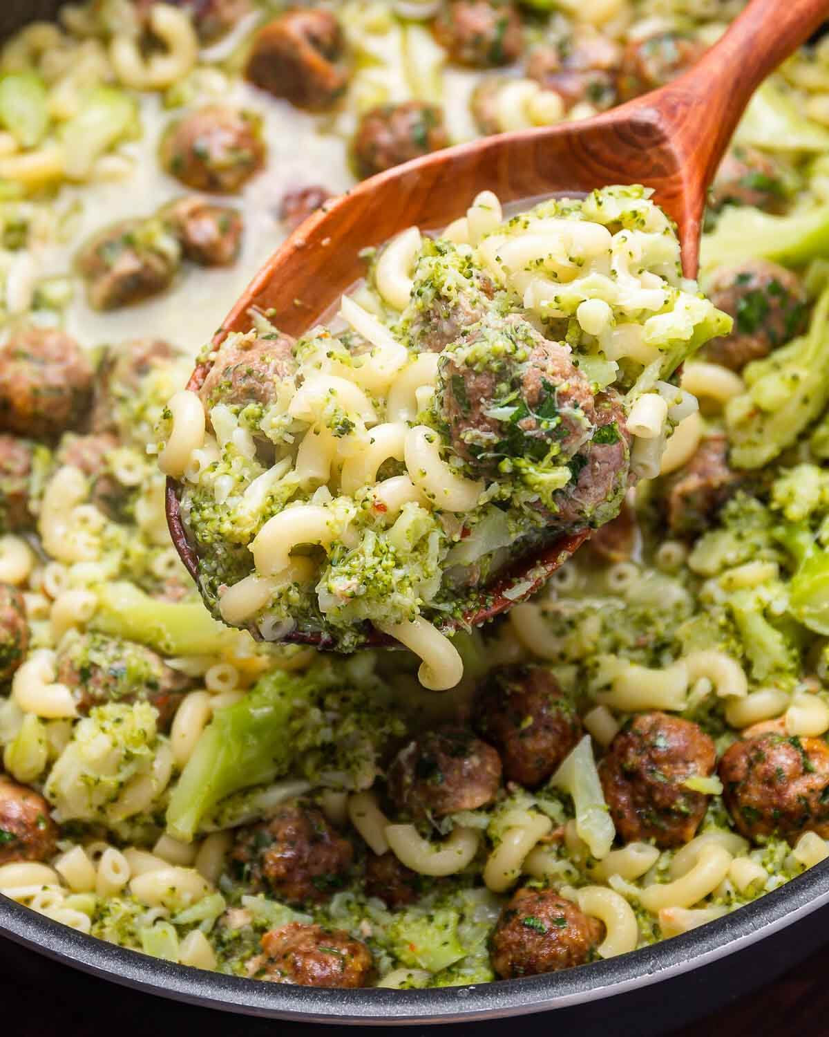 Large wooden spoon holding macaroni with broccoli and meatballs.