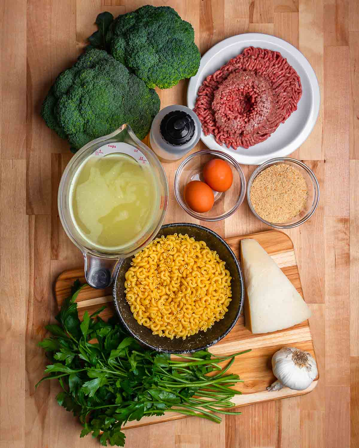 Ingredients shown: broccoli, ground beef, olive oil. chicken stock, eggs, breadcrumbs, macaroni, cheese, garlic, and parsley.