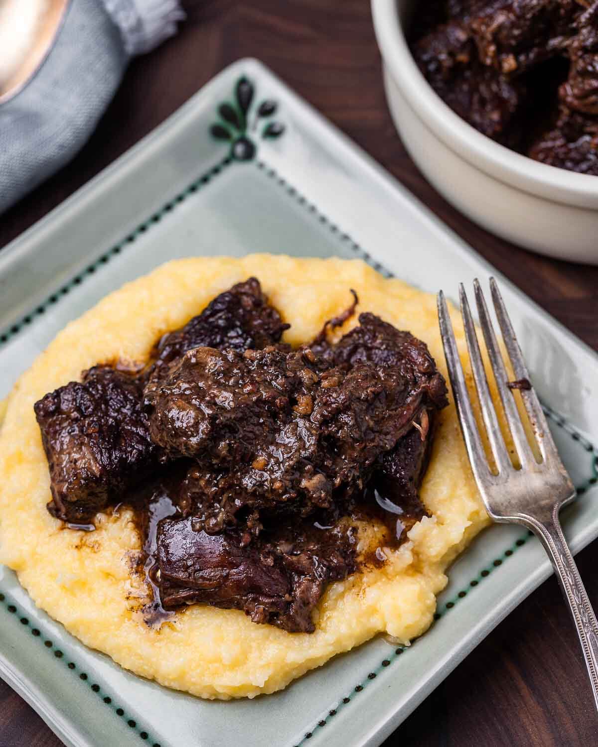 Blue plate with Tuscan beef stew on polenta and fork.