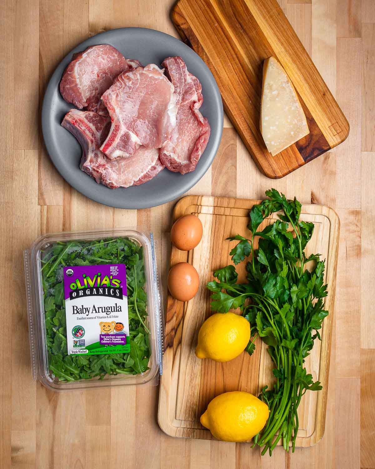 Ingredients shown: pork chops, Parmigiano Reggiano, baby arugula, eggs, lemons, and parsley.