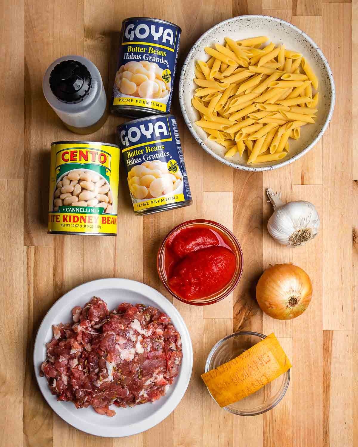 Ingredients shown: olive oil, beans, penne, tomatoes, bulk Italian sausage, Parmigiano rind, onion, and garlic.