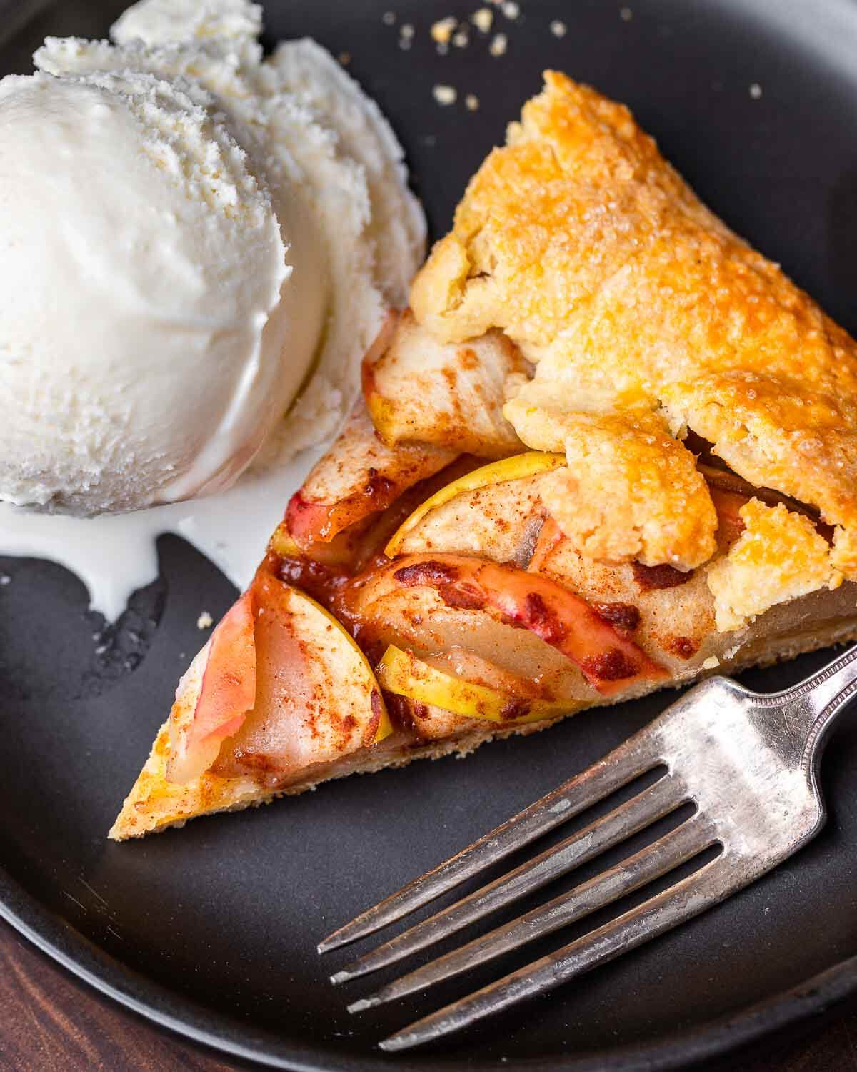 Slice of apple crostata and vanilla ice cream on black plate.