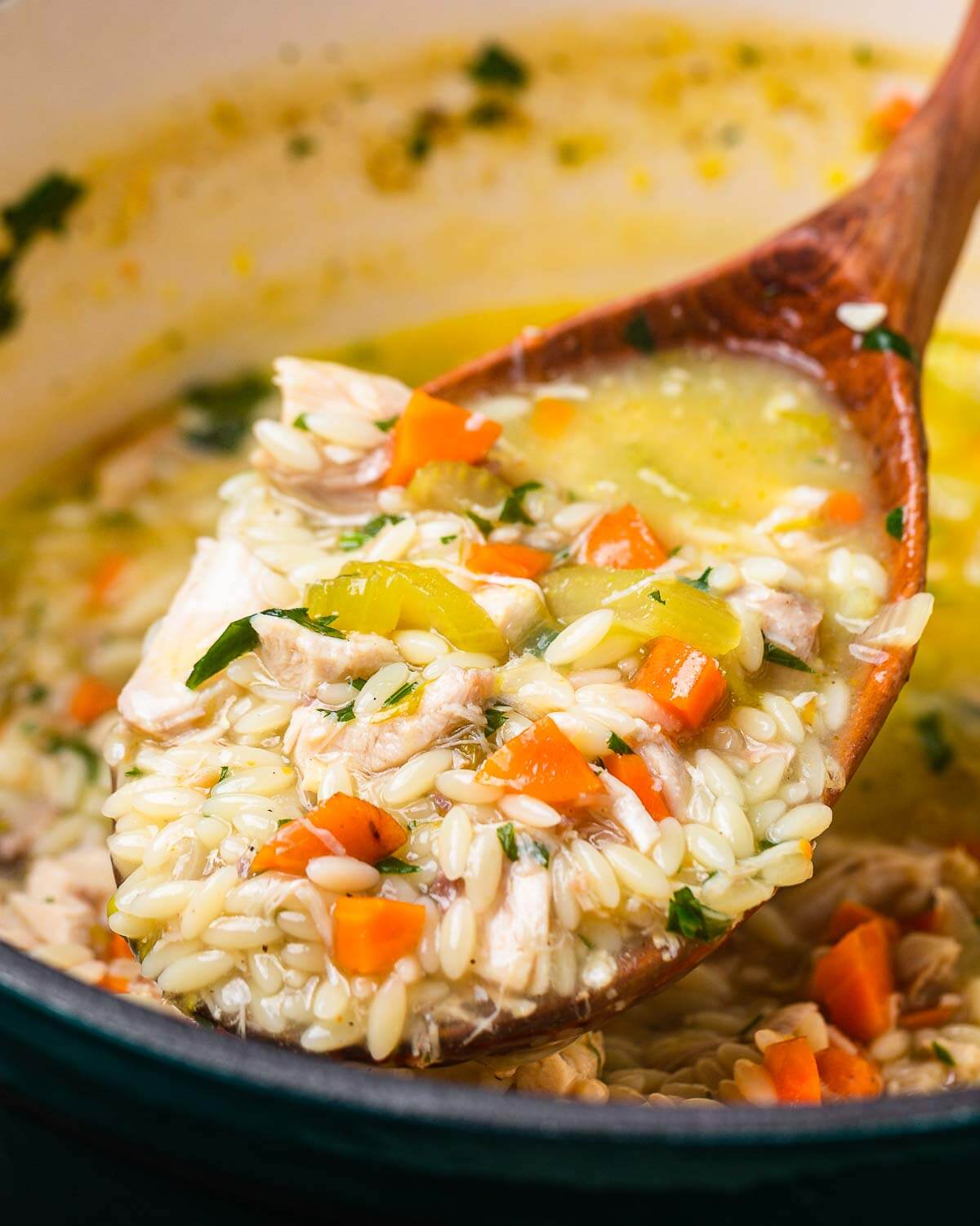 Large wooden ladle holding lemon chicken orzo soup over pot.