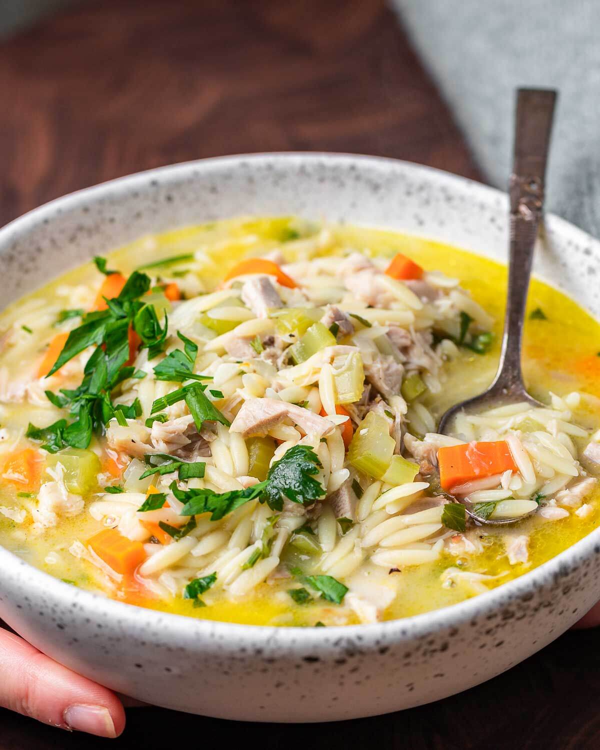 Hands holding bowl of lemon chicken orzo soup.