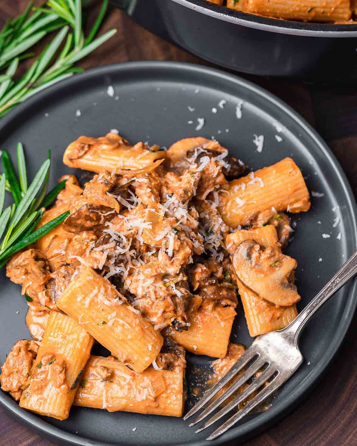 Pasta boscaiola in grey plate with rosemary garnish.