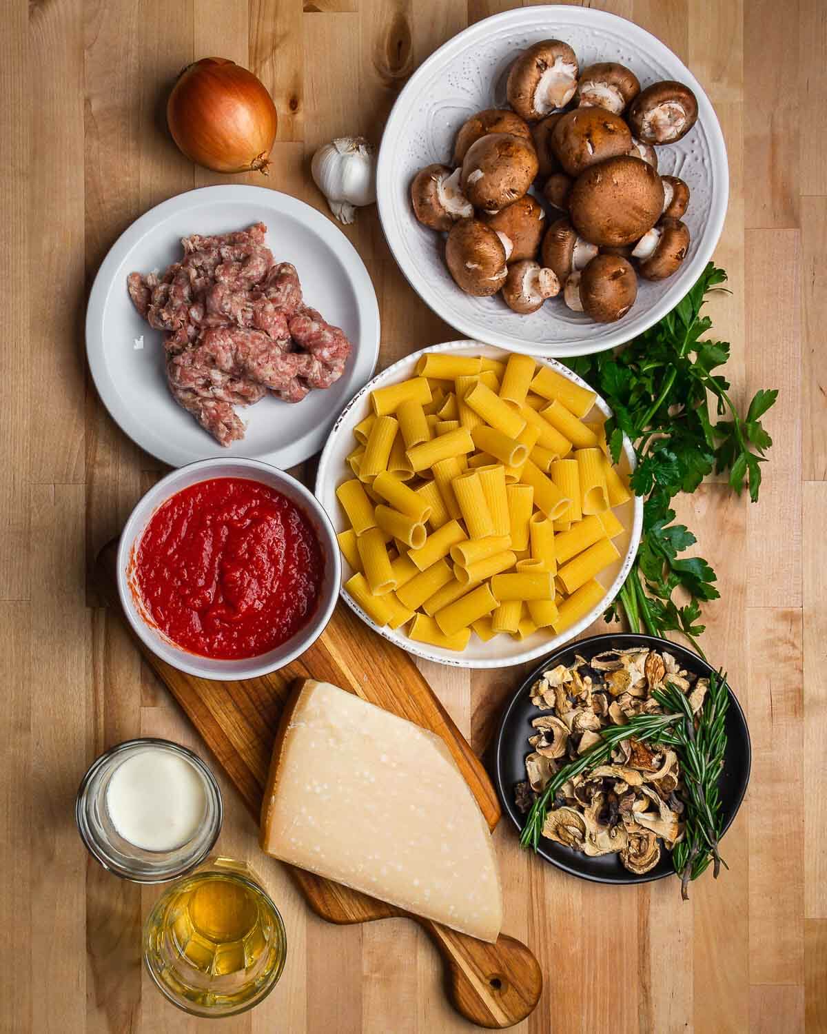 Ingredients shown: onion, garlic, mushrooms, rigatoni, parsley, plum tomatoes, rosemary, cream, white wine, and Parmigiano Reggiano.