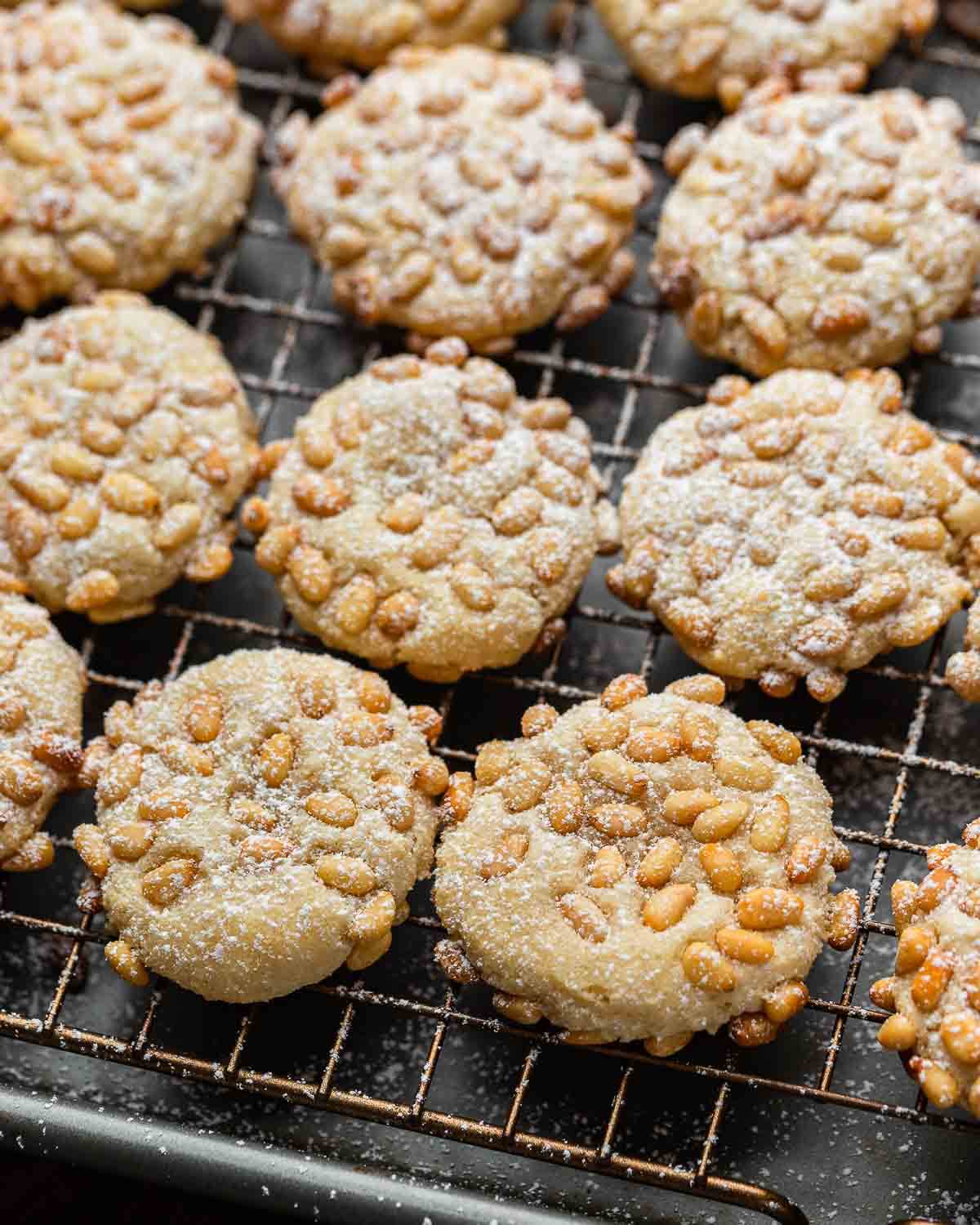 Baked pignoli cookies on grey wire rack.