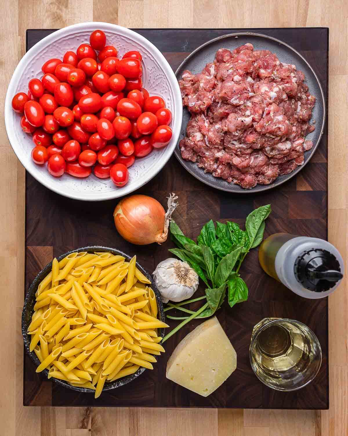 Ingredients shown: cherry tomatoes, bulk sausage, onion, garlic, basil, olive oil, white wine, Pecorino Romano, and penne pasta.
