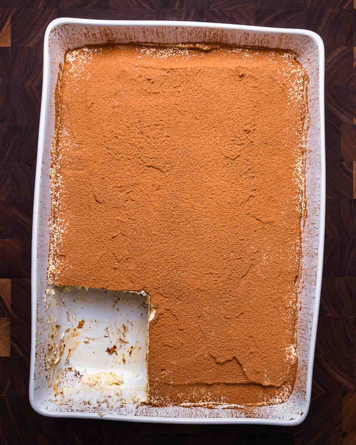 Tiramisu in white baking dish with piece cut out of it.