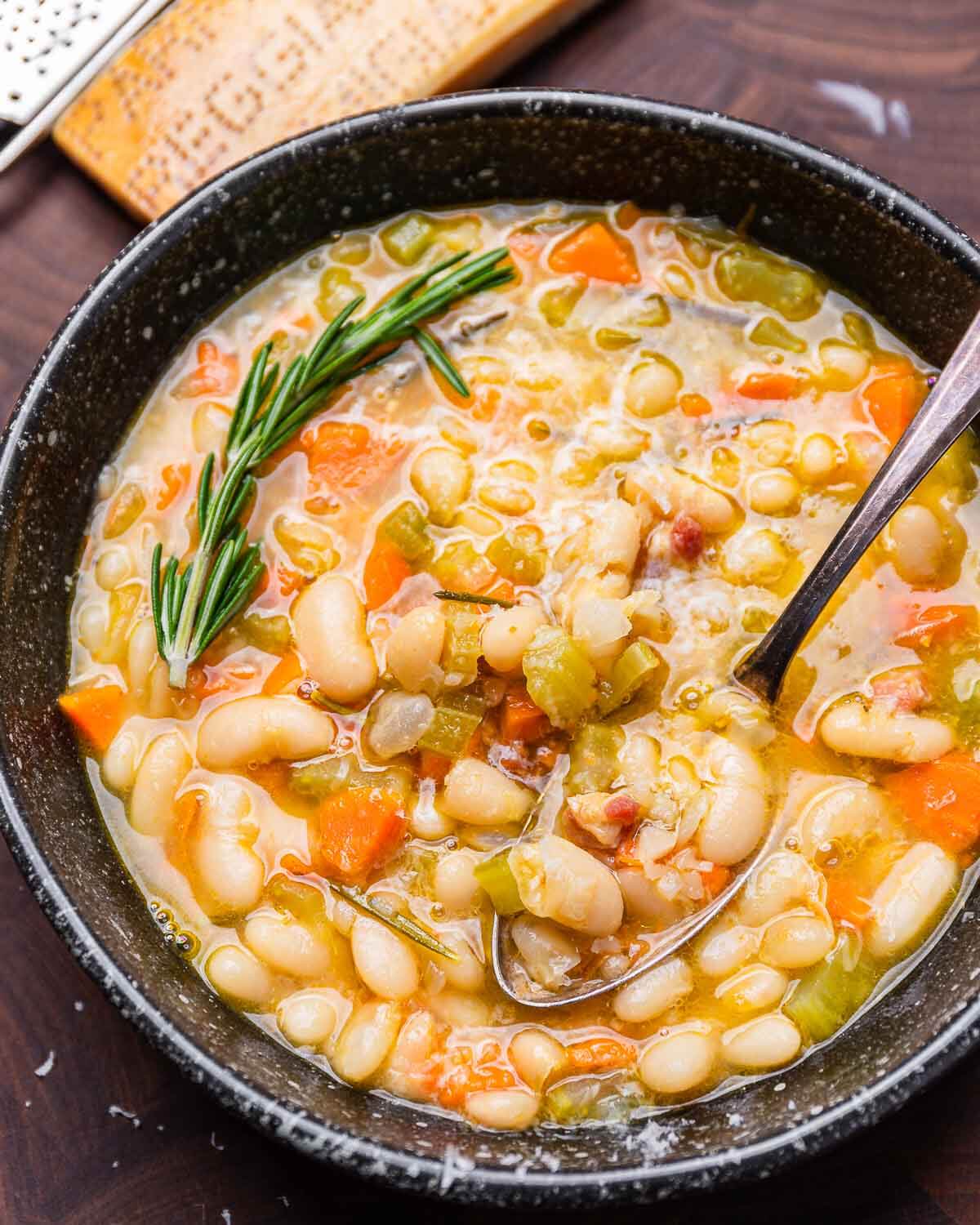 Tuscan white bean soup in black bowl with Parmigiano Reggiano block in background.